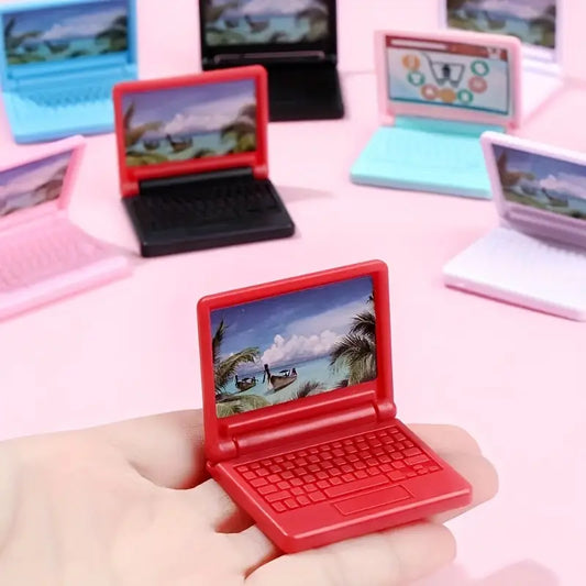 Red toy laptop held in a hand with other similar laptops in the background on a pink surface.